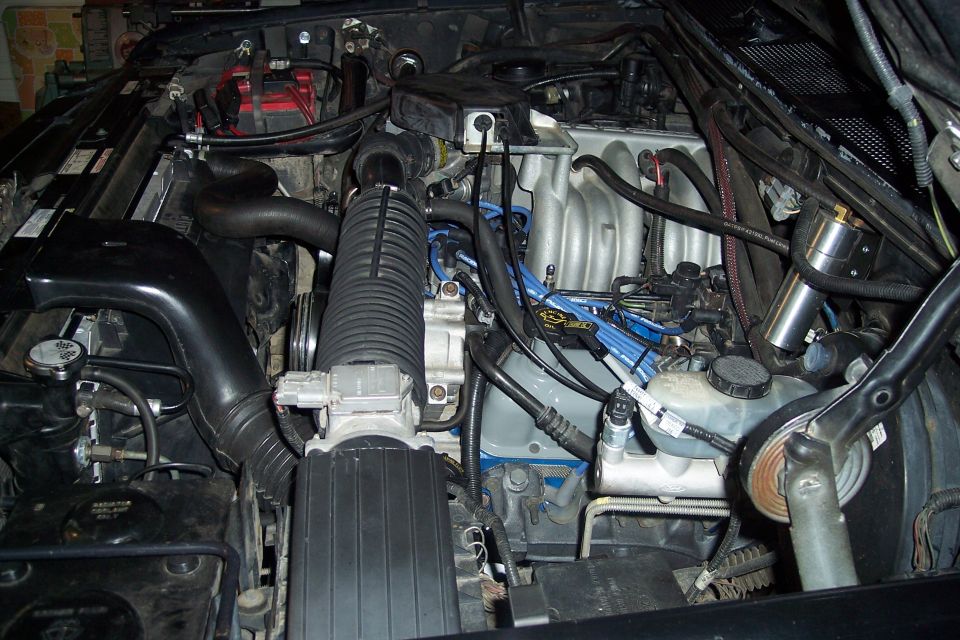 Engine bay with air intake, battery, and engine components visible. Some blue spark plug wires are prominent