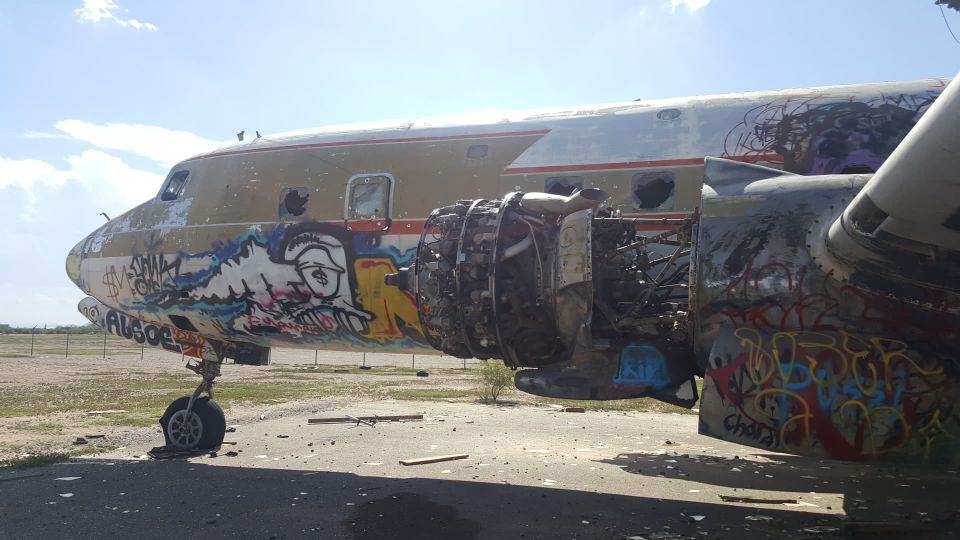 Graffiti-covered airplane with exposed engine, parked on tarmac