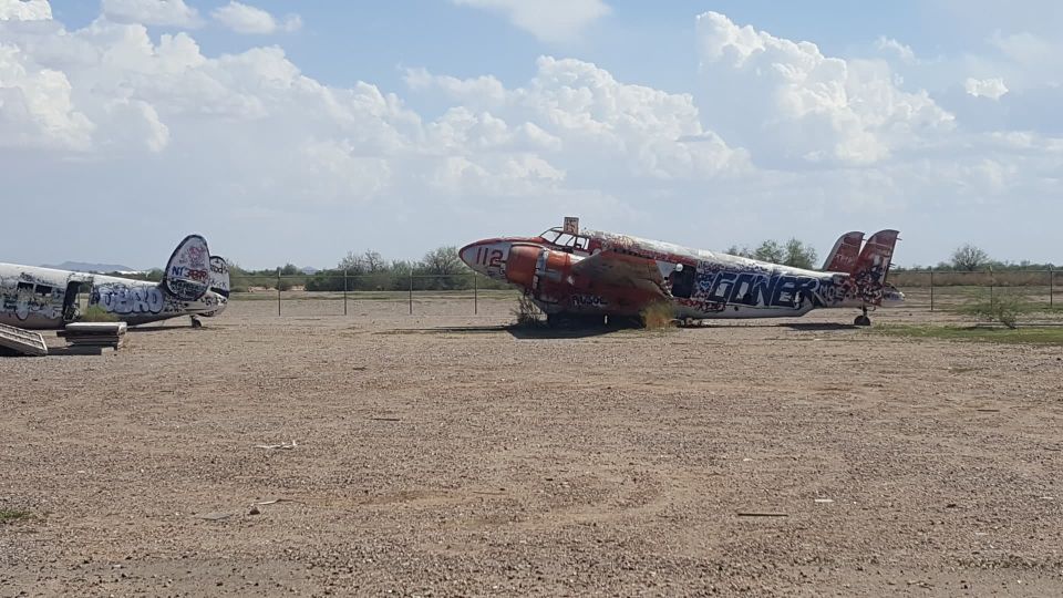 Two graffiti-covered airplanes sit in a dusty field under a cloudy sky. One plane has 'GONER' painted on its side