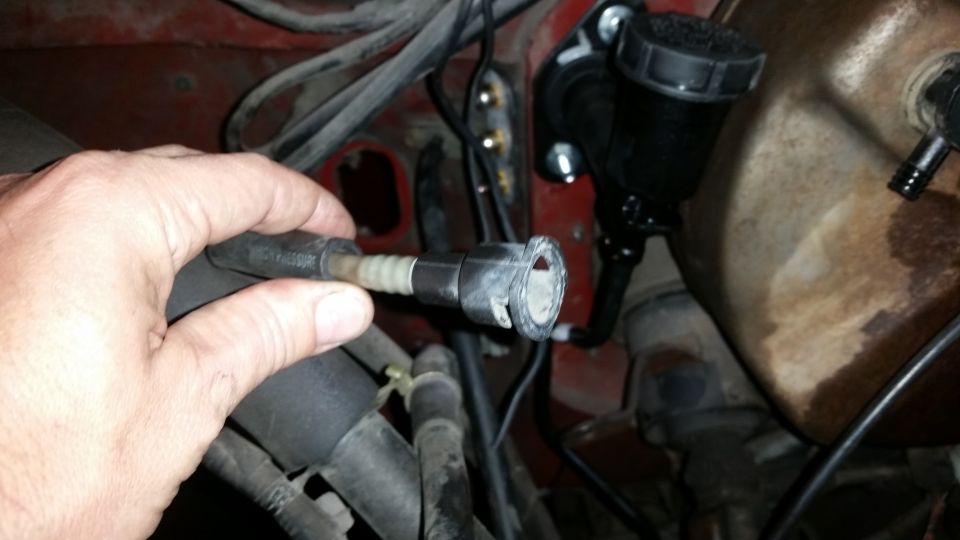 Hand holding a disconnected brake line near the master cylinder reservoir