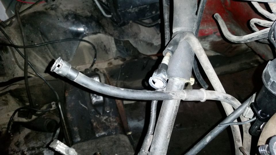 Engine bay with disconnected fuel line and various hoses. Red paint visible