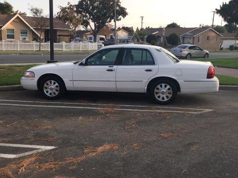 1989 Mazda MX-6 - A white sedan is parked in a lot with houses in the background. Another car is visible on the street.