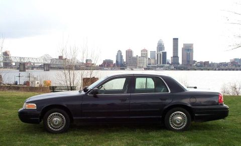 1998 Ford Crown Victoria - Side view of a 1998 Ford Crown Victoria parked by a river with a city skyline.