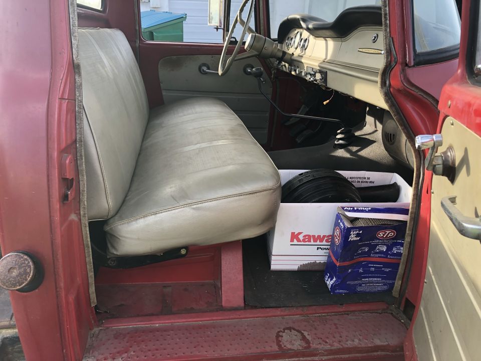 Interior of a red truck cab showing a tan bench seat, dashboard, and floor with parts.