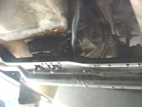 1988 Ford Bronco - The underside of a vehicle reveals a transmission and oil pan, with visible signs of fluid leaks.