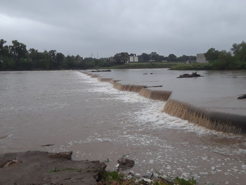 River with a low dam and murky water under an overcast sky.