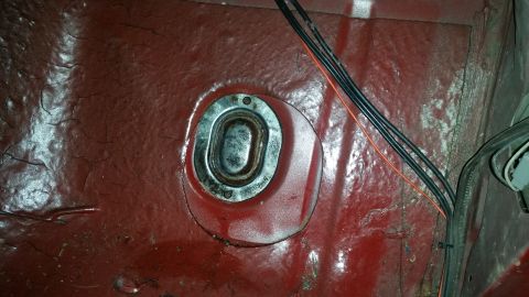 1985 Ford Bronco - A close-up view of the interior floor of a vehicle, showing a metal grommet with screws and some wiring. The red painted floor shows signs…