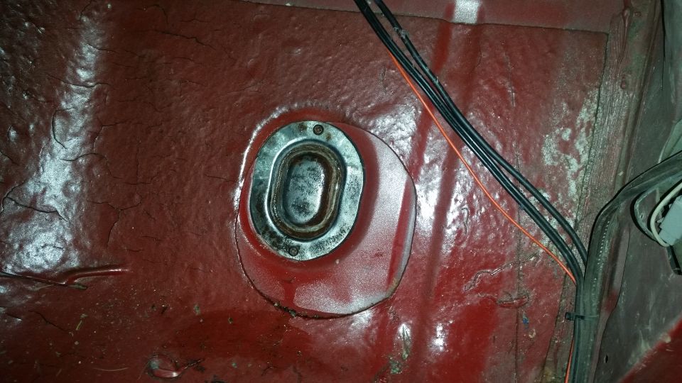 Interior vehicle floor with metal grommet and wiring, red paint with cracks.