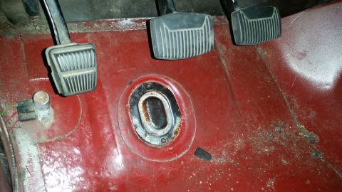 1985 Ford Bronco - The interior floor of a vehicle shows three pedals: clutch, brake, and accelerator. A circular metal plate with an oval opening is visible…