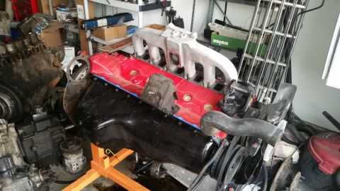 1985 Ford Bronco - A disassembled V8 engine is on an orange engine stand, with the intake manifold and valve covers removed, revealing the cylinder heads. The…