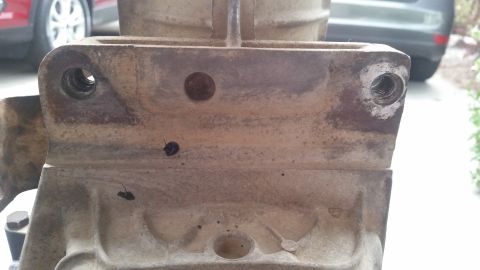 1985 Ford Bronco - A close-up view of a heavily weathered metal component, likely part of a vehicle's transmission or drivetrain, showing threaded bolt holes…