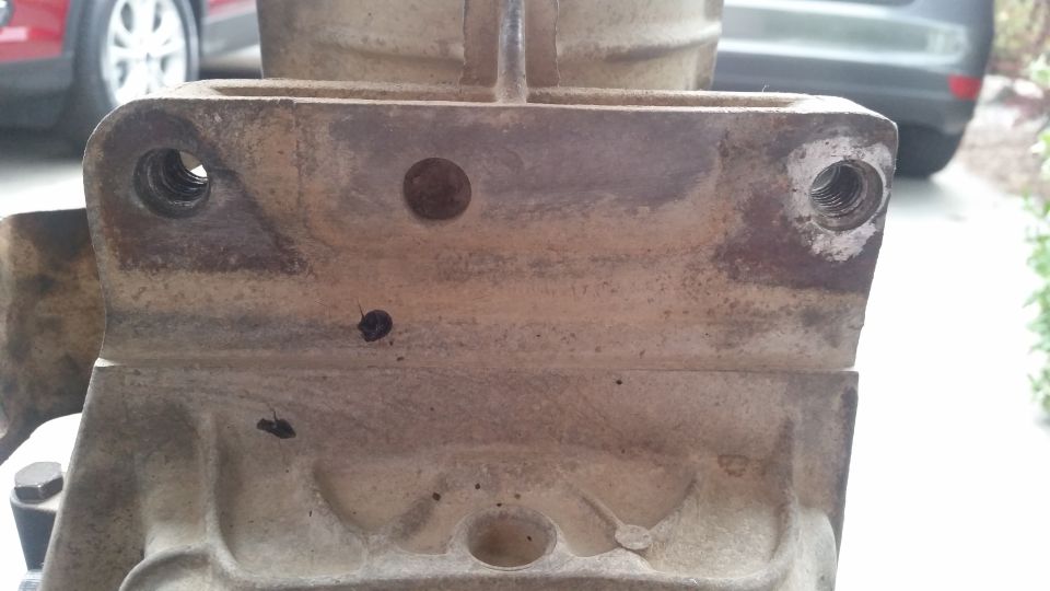Close-up of weathered metal vehicle part with threaded holes.