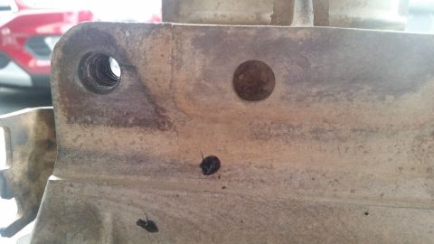 1985 Ford Bronco - A close-up view of a heavily weathered, possibly cast metal automotive part with two holes. One hole on the left is threaded, while a small…
