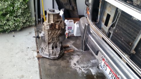 1985 Ford Bronco - A disassembled transmission is resting on wooden blocks on a concrete driveway next to a vehicle's front end. The vehicle appears to be a t…
