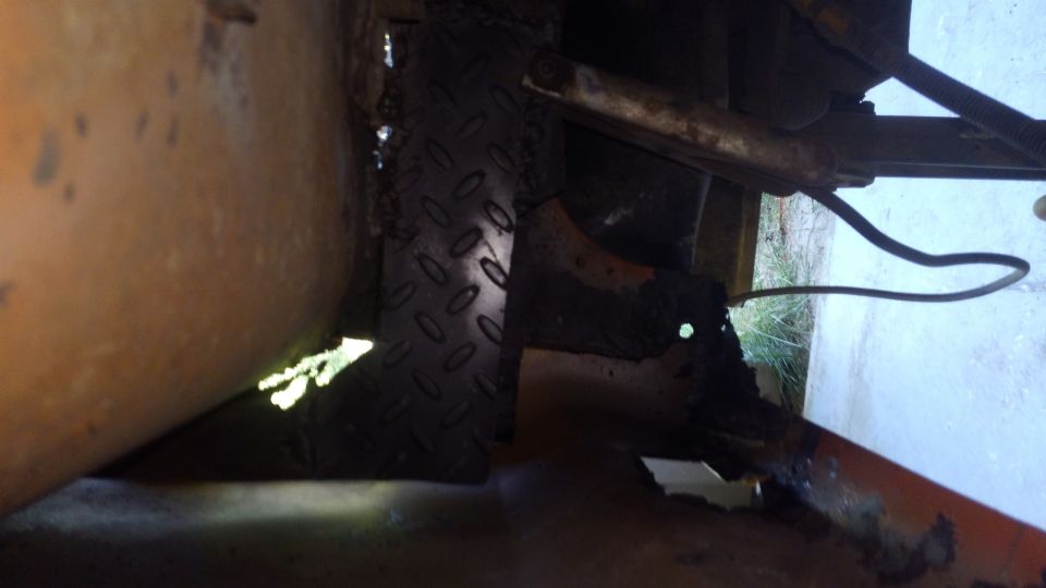 Close-up of rusty undercarriage with diamond plate and hose.