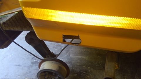 1996 Ford Bronco - A close-up view shows a rectangular hole cut into the yellow plastic body panel of a vehicle, likely a bumper or fender. The hole reveals s…