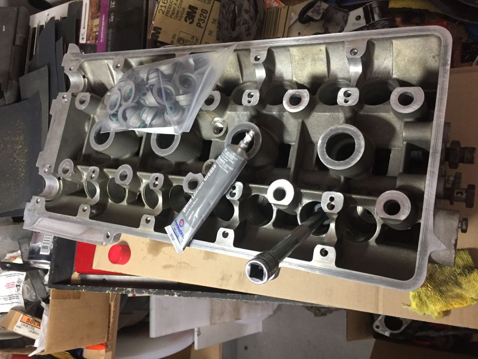 Disassembled engine cylinder head with valve seals, grease, and socket wrench.