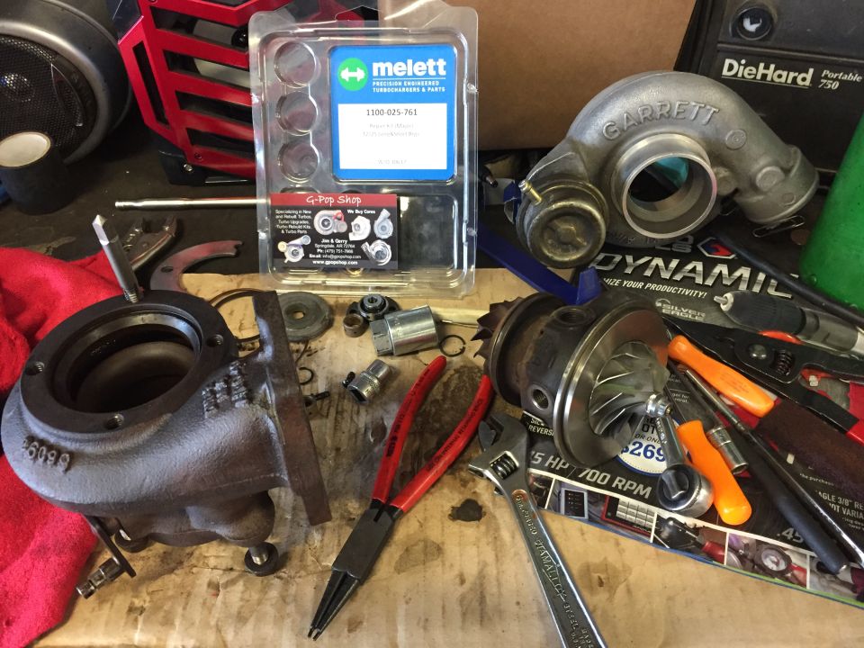 Disassembled turbocharger with repair kit and tools on a workbench.
