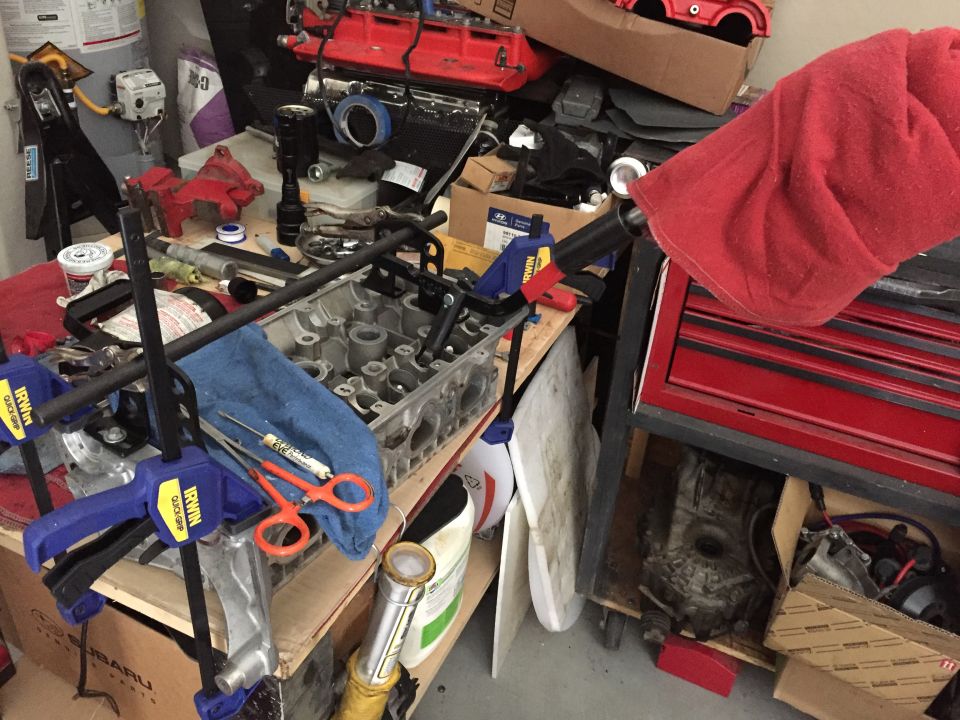Engine cylinder head clamped to a workbench with tools and a red toolbox.