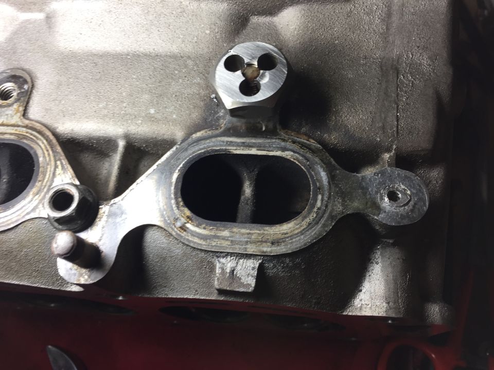 Engine block with exhaust manifold gaskets and a three-hole metal component.