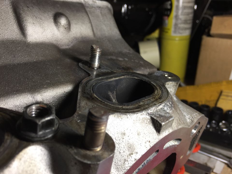 Close-up of a vehicle engine cylinder head with gasket surface, bolt stud, and nut.