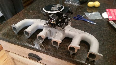 1985 Ford Bronco - A silver Offenhauser intake manifold with a black throttle body assembly is shown on a granite countertop. The manifold has four intake por…