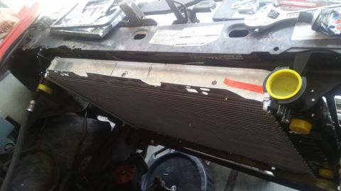 1985 Ford Bronco - A close-up, angled view shows a new radiator being installed in the engine bay of a vehicle. Tools and parts are visible in the background,…