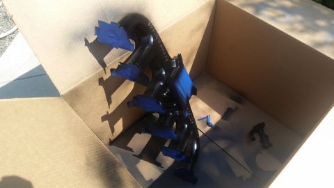 1985 Ford Bronco - A black exhaust manifold, partially covered with blue painter's tape, sits inside a cardboard box. Spray paint marks are visible on the bot…