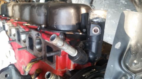 1985 Ford Bronco - The image shows a close-up view of a red engine block with a black valve cover. A metal pipe extends from a black fitting attached to the e…