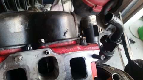 1985 Ford Bronco - A close-up view of a black engine valve cover with red paint on the manifold underneath. A black metal pipe with a curved end is attached t…
