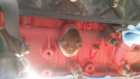 1985 Ford Bronco - A close-up view of a red engine block with a dark, triangular plate secured by two bolts. The engine appears to be part of a vehicle restor…