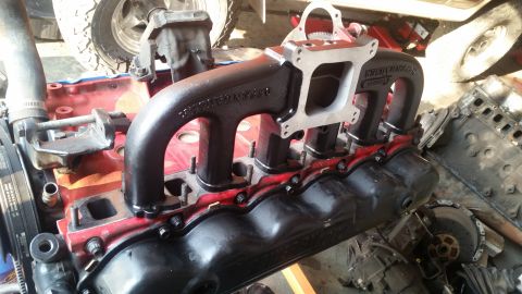 1985 Ford Bronco - A close-up view of a black aftermarket intake manifold bolted onto a red engine block. The manifold has "EDELBROCK" stamped on it, and a si…