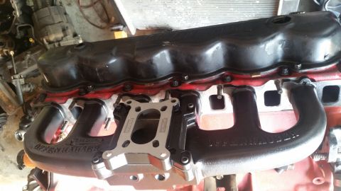1985 Ford Bronco - Engine cylinder head intake manifold with valve cover and a four-barrel carburetor adapter plate sitting on a workbench.