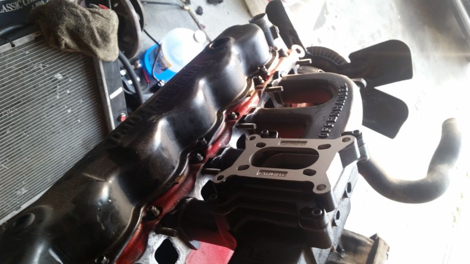 Close-up of a black engine manifold with carburetor spacer and fan.