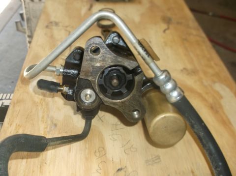 1979 Ford Ranchero - A close-up view of a power steering pump with a metal line and a black hose attached, resting on a wooden surface. The pump has a black met…