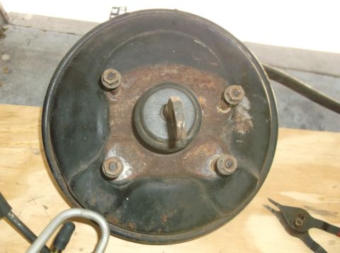 1979 Ford Ranchero - A close-up, overhead view of a rusty, black brake booster assembly with four bolts visible. A metal rod protrudes from the center of the as…
