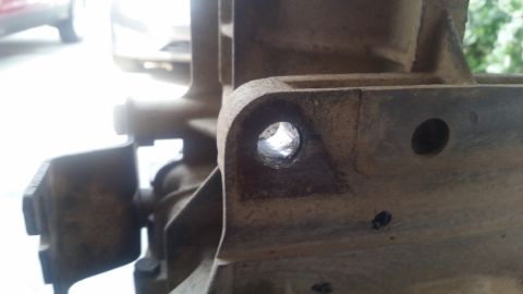 1985 Ford Bronco - A close-up view shows a hole drilled into a dirty, cast metal automotive part, likely a transmission or transfer case housing. The hole app…