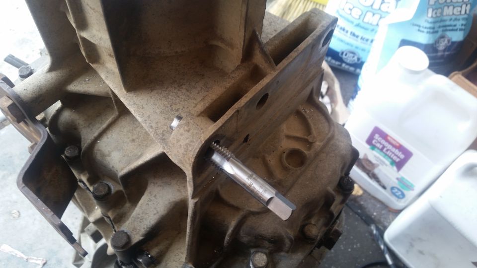 Close-up of a tap threading a hole in a dirty transmission housing.