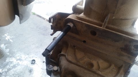 1985 Ford Bronco - A close-up view shows a hex bit tool inserted into a threaded hole on a dirty, cast-iron automotive transmission housing. The tool is angle…