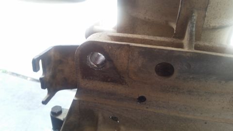 1985 Ford Bronco - Close-up view of a heavily soiled metal component with a threaded hole. Another smaller hole is visible to the right, and a bracket with a…