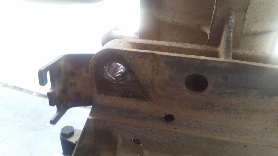 Close-up of a dirty metal part with a threaded hole and a bracket.