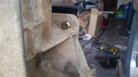 1985 Ford Bronco - A close-up view shows a golden bolt securing a metal bracket to a heavily weathered, tan-colored vehicle component. The background is blurr…