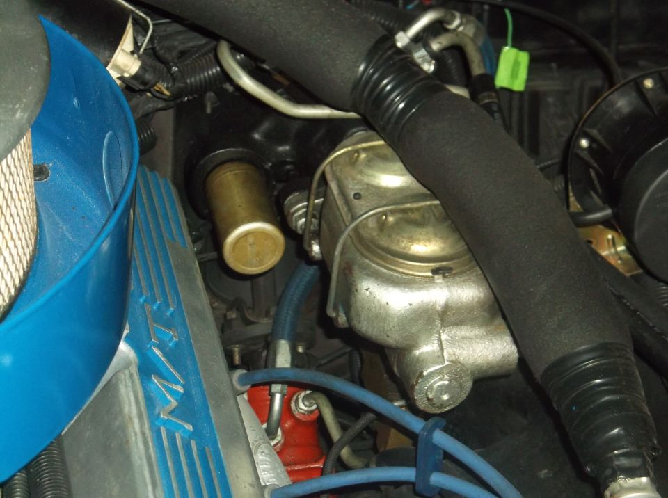 Close-up of engine bay showing brake booster, master cylinder, blue air intake, and valve cover.