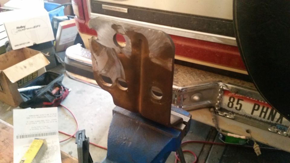 Rusty metal bracket clamped in a vise, with a license plate visible in the background.