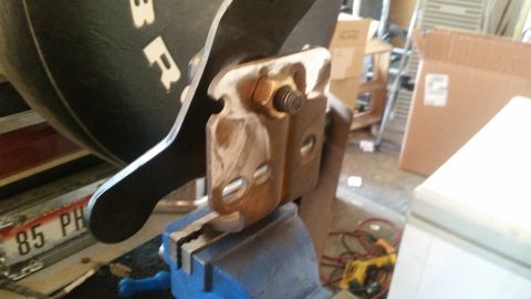 1985 Ford Bronco - A close-up shot shows a metal bracket being held in a blue vise, attached to a black object with white lettering. A license plate with "85…