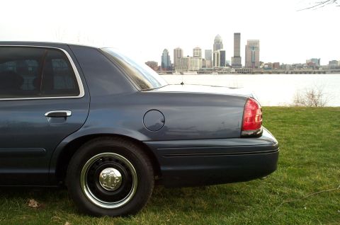 1998 Ford Crown Victoria - A dark blue sedan is parked on a grassy hill overlooking a city skyline and a body of water.