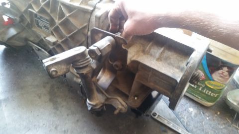 1985 Ford Bronco - A hand is shown adjusting a metal bracket attached to a dirty, cast-aluminum transmission housing. The transmission appears to be from a tr…