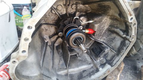 1985 Ford Bronco - A close-up view of the inside of a transmission bell housing, showing a clutch release bearing assembly with a spring and hydraulic line at…
