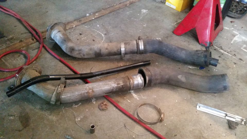 Two exhaust pipes with clamps and a black flexible hose on a concrete floor.