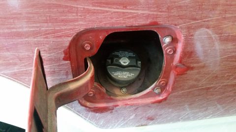1985 Ford Bronco - The image shows a close-up view of an open red fuel filler door on a vehicle. Inside the opening, a black gas cap with white text is visibl…